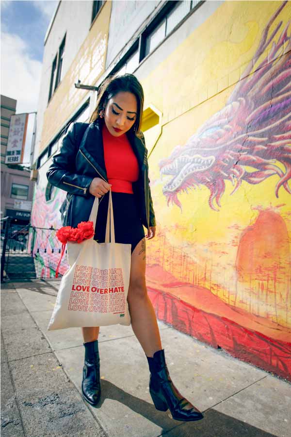 Asian woman holding tote bag that reads: Love Over Hate
