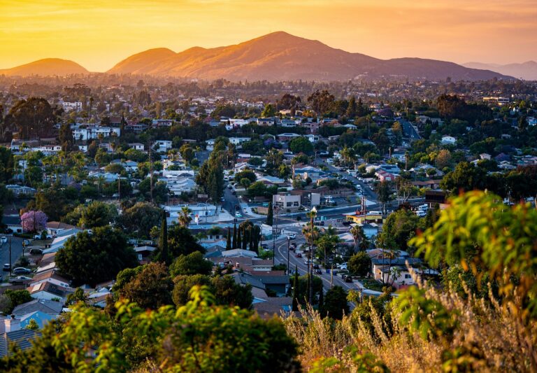 Documentjpeg - Harborside A suburban neighborhood with houses and streets, surrounded by trees, at sunset with mountains visible in the background. Documentjpeg