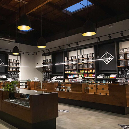 San-Ysidro-thumbjpg - Harborside Modern retail store interior with wooden display counters, shelves stocked with products, dark pendant lighting, and industrial ceiling design. San-Ysidro-thumbjpg