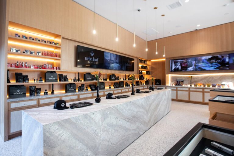 Urbn-Leaf-West-Hollywood-Los-Angelese-Cannabis-Dispensary-Sunset-Strip-Interior-3jpg - Harborside Modern retail store interior with light wood shelves displaying various products, a marble counter in the center, and digital screens on the walls. Urbn-Leaf-West-Hollywood-Los-Angelese-Cannabis-Dispensary-Sunset-Strip-Interior-3jpg