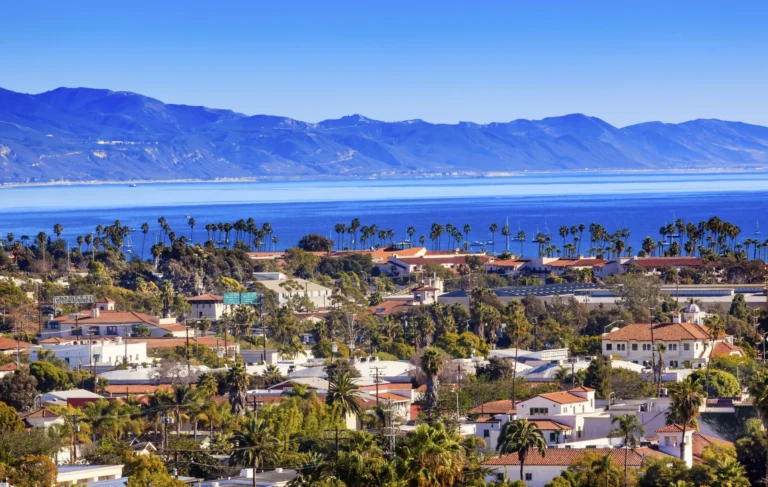 adddf0af521093fa2716a30e4ca56cb6-scaledwebp - Harborside A coastal cityscape with palm trees, residential buildings, and the ocean in the background, set against distant mountains under a clear blue sky. adddf0af521093fa2716a30e4ca56cb6-scaledwebp