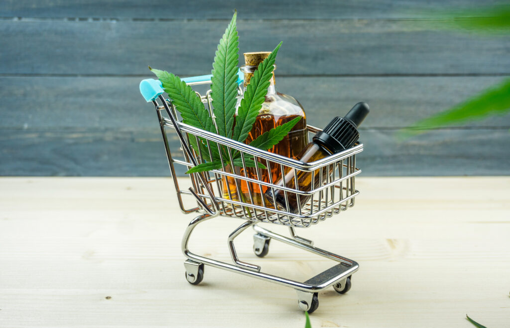 Supermarket trolley with marijuana leafs and medical cannabis oil cbd on wooden backdrop